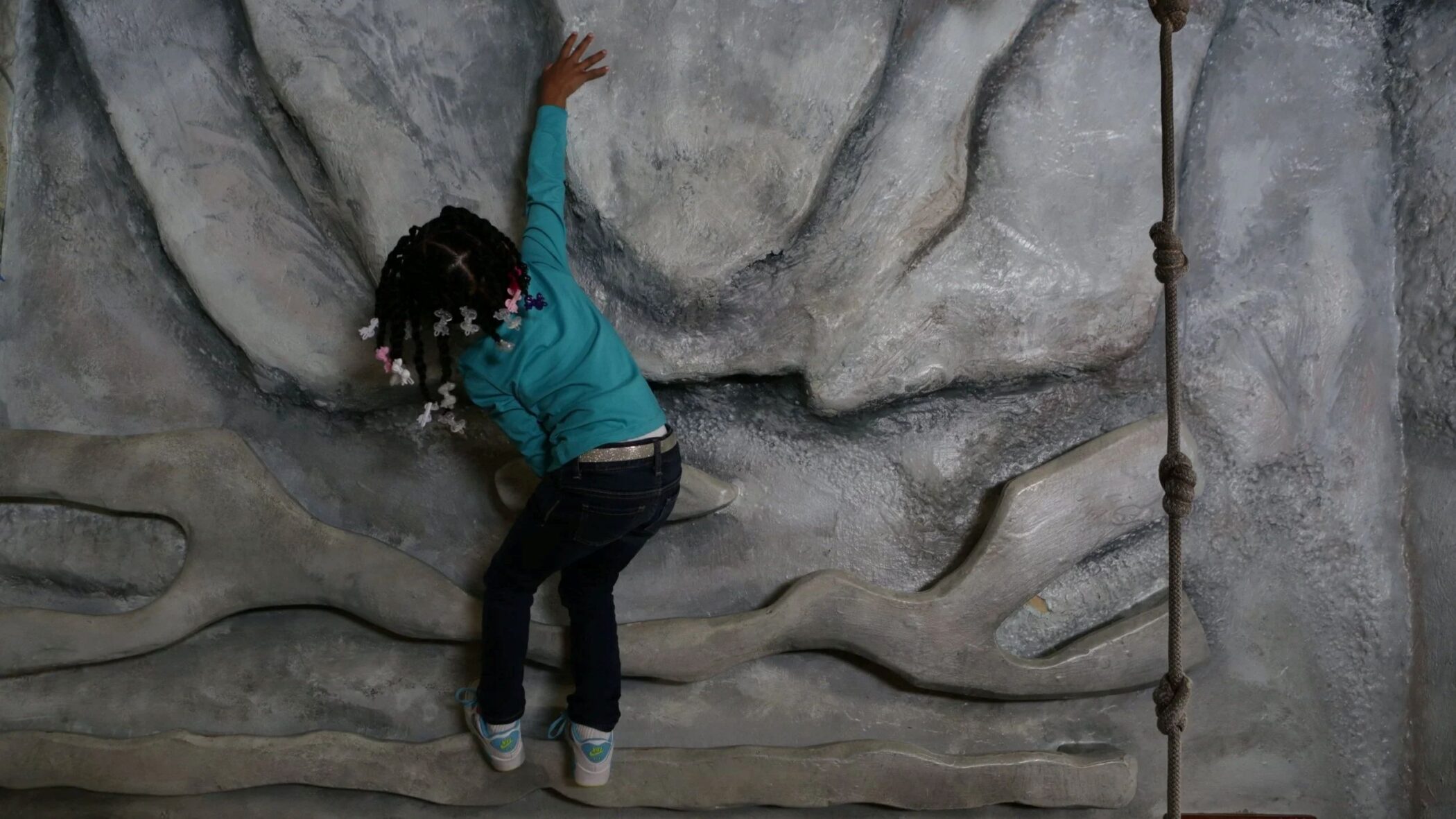Child climbing a textured rock wall in the Treehouse Trails exhibit