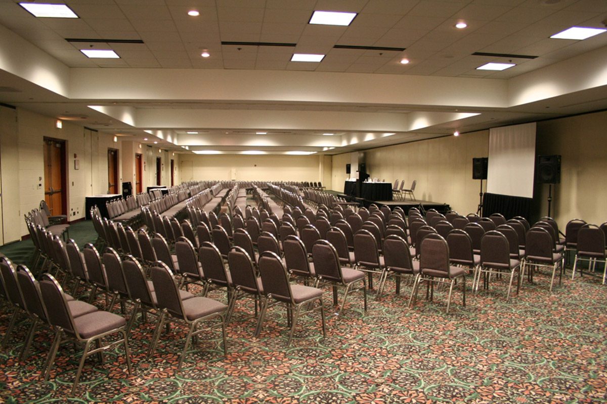 Large Meeting Space With Rows Of Seats And An Elevated Presentation Area