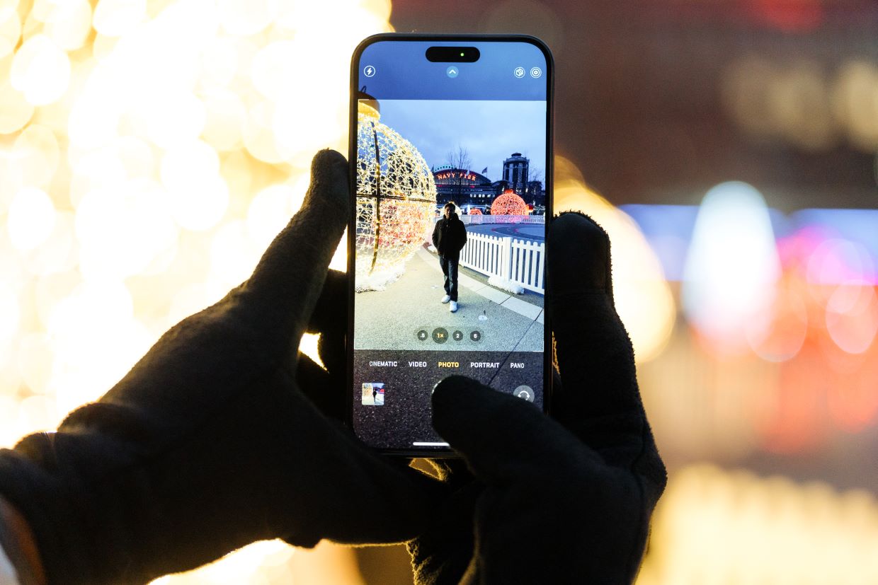 person holding iphone taking photo of friend next to holiday lights
