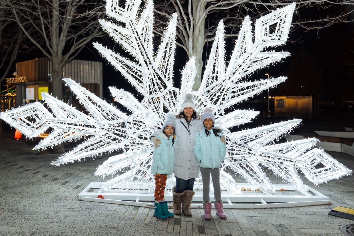 Mom and daughters outside in front of giant snowflake light display