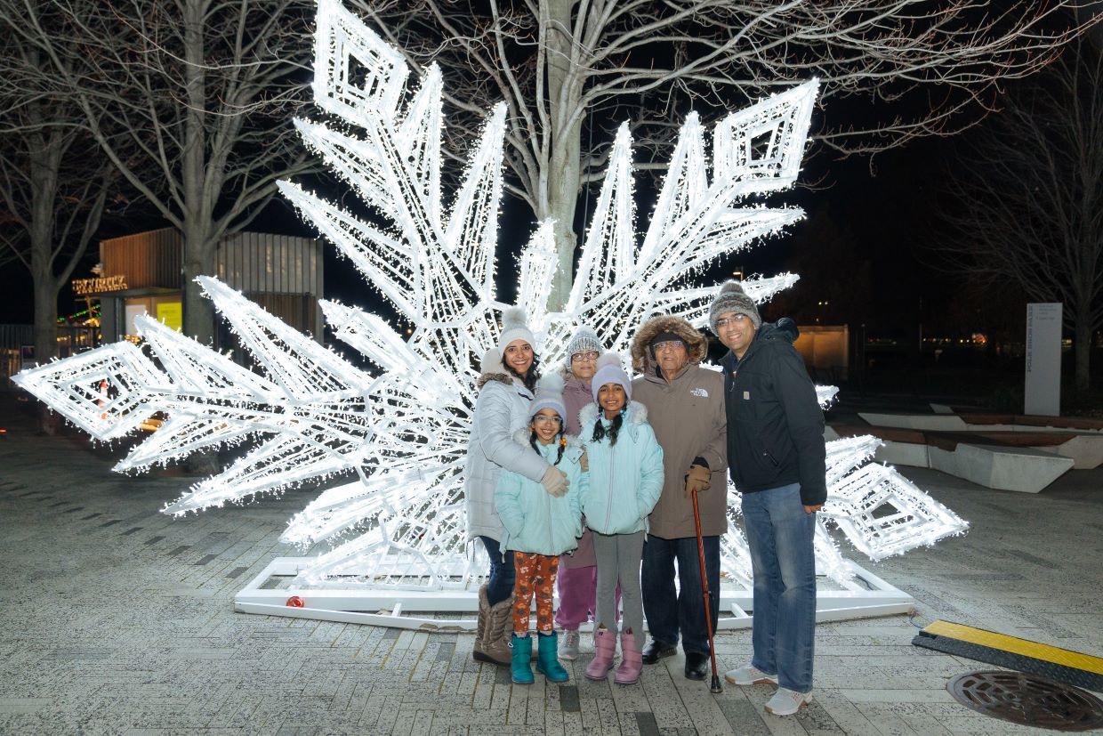 family standing in front of giant white light snowflake lights at night