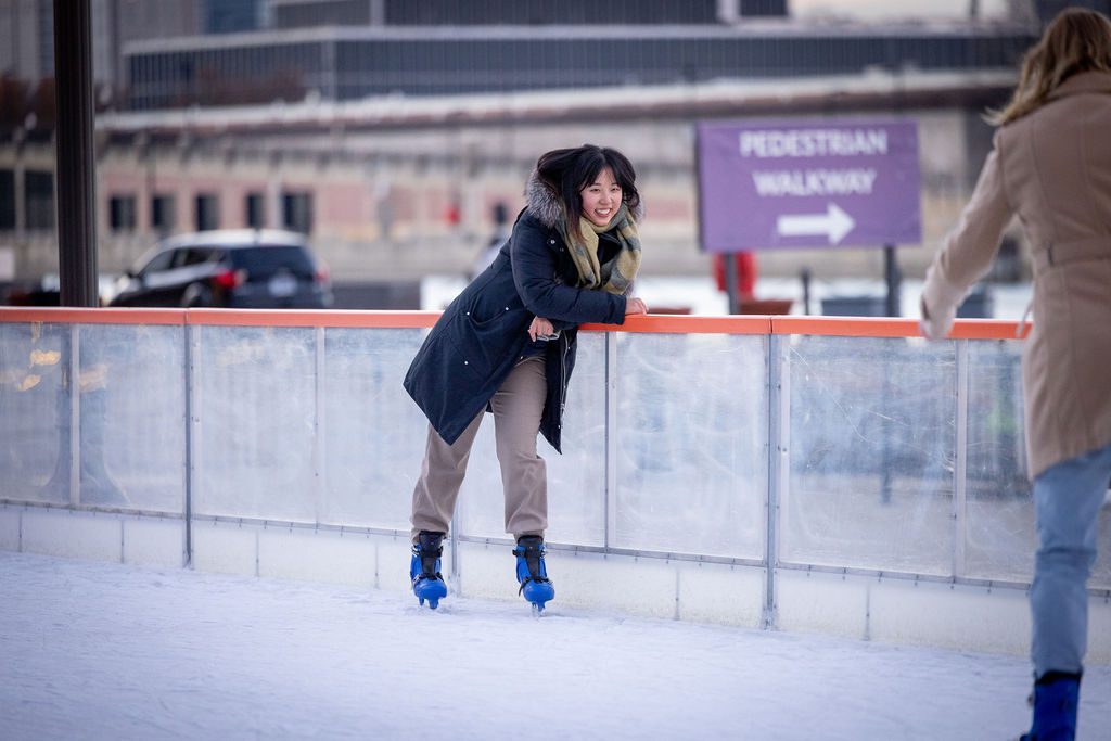 woman in grey coat leaning against ice skating rink wall