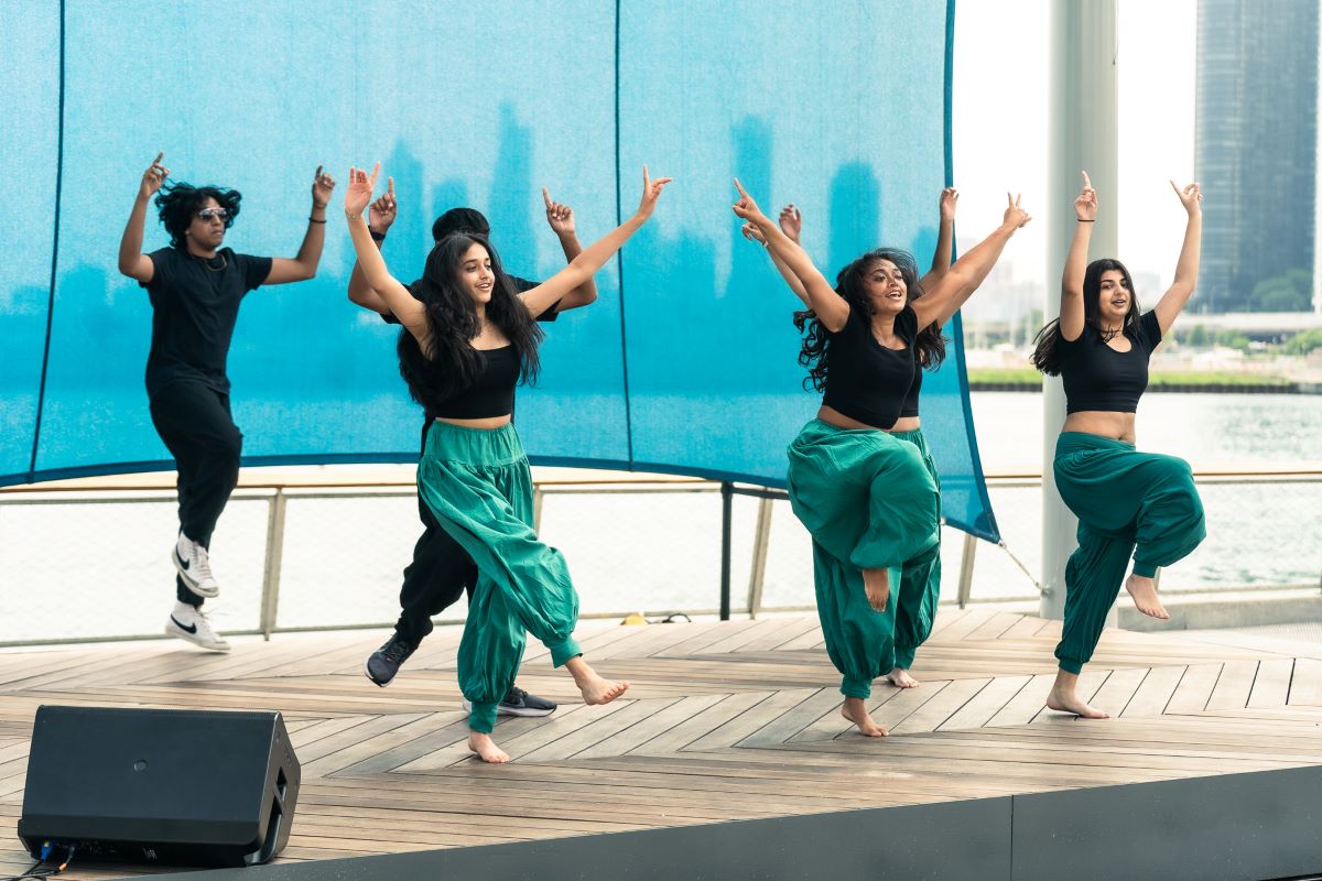 A lively group of young kids dancing on a dock, celebrating together against a backdrop of water and sunshine
