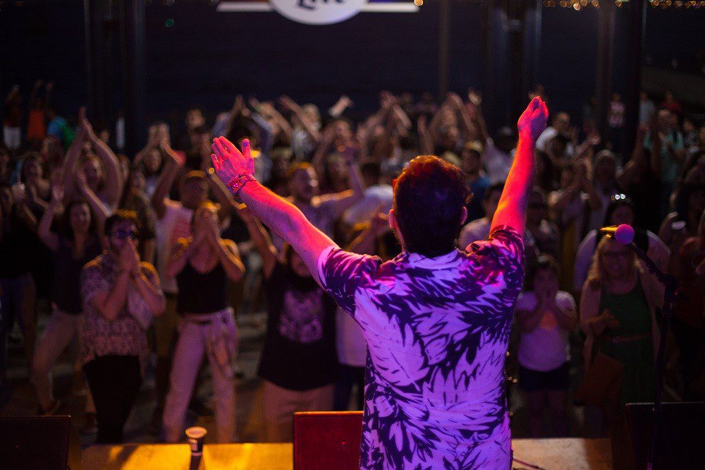 Performer on stage with arms raised facing a cheering crowd