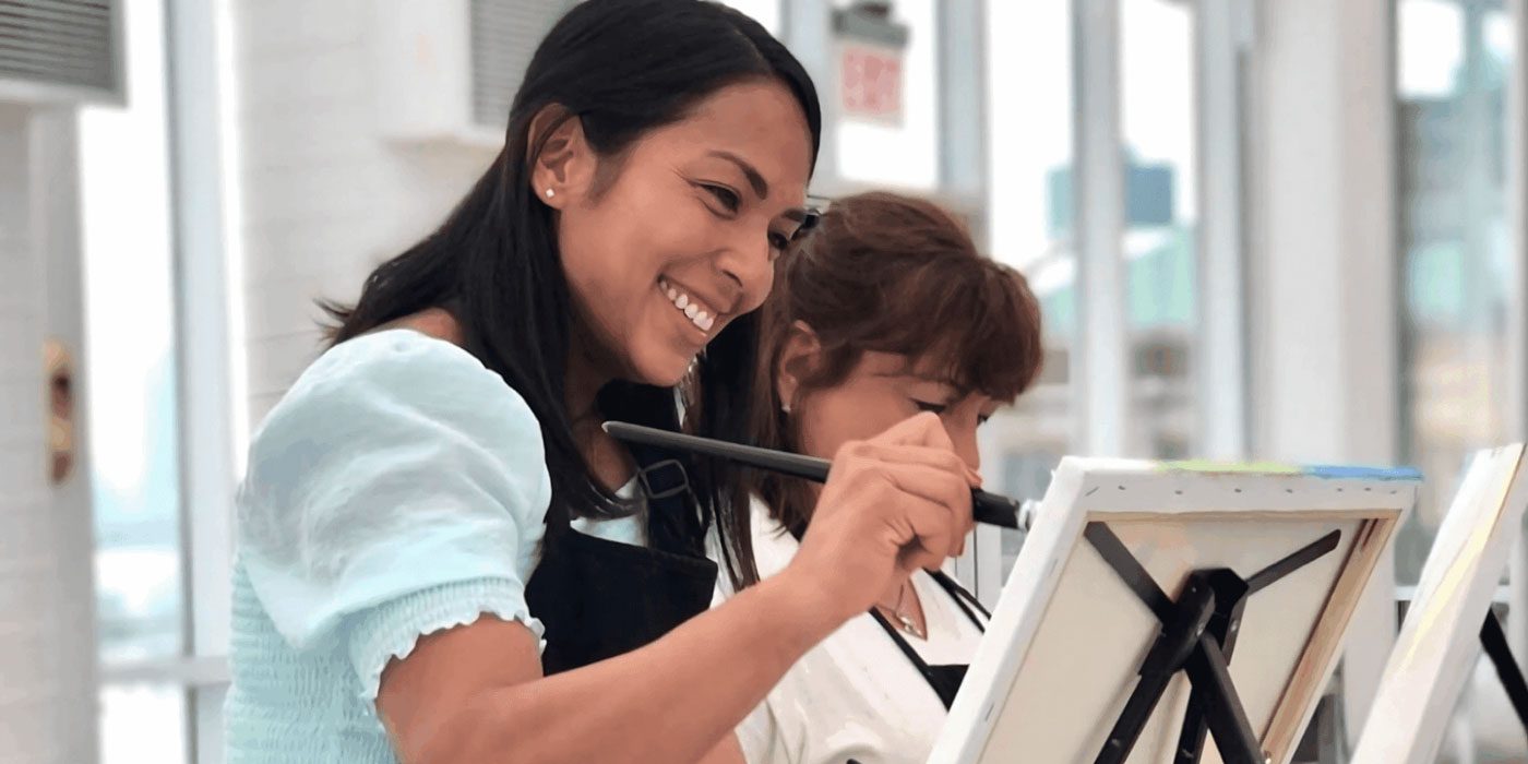 People seated at tables painting on canvases during a group art activity