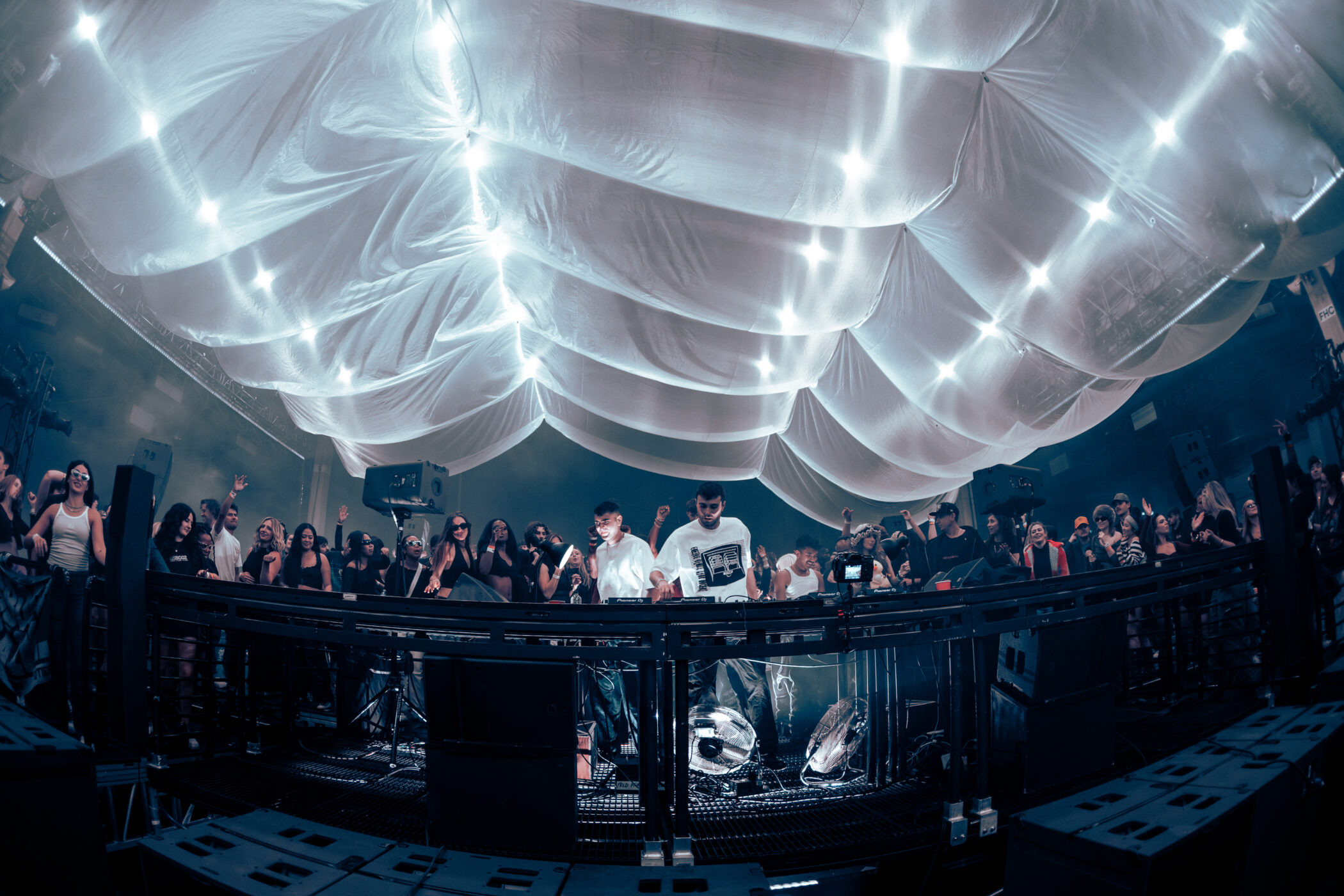 fred again performing at a central booth surrounded by a crowd under a fabric ceiling