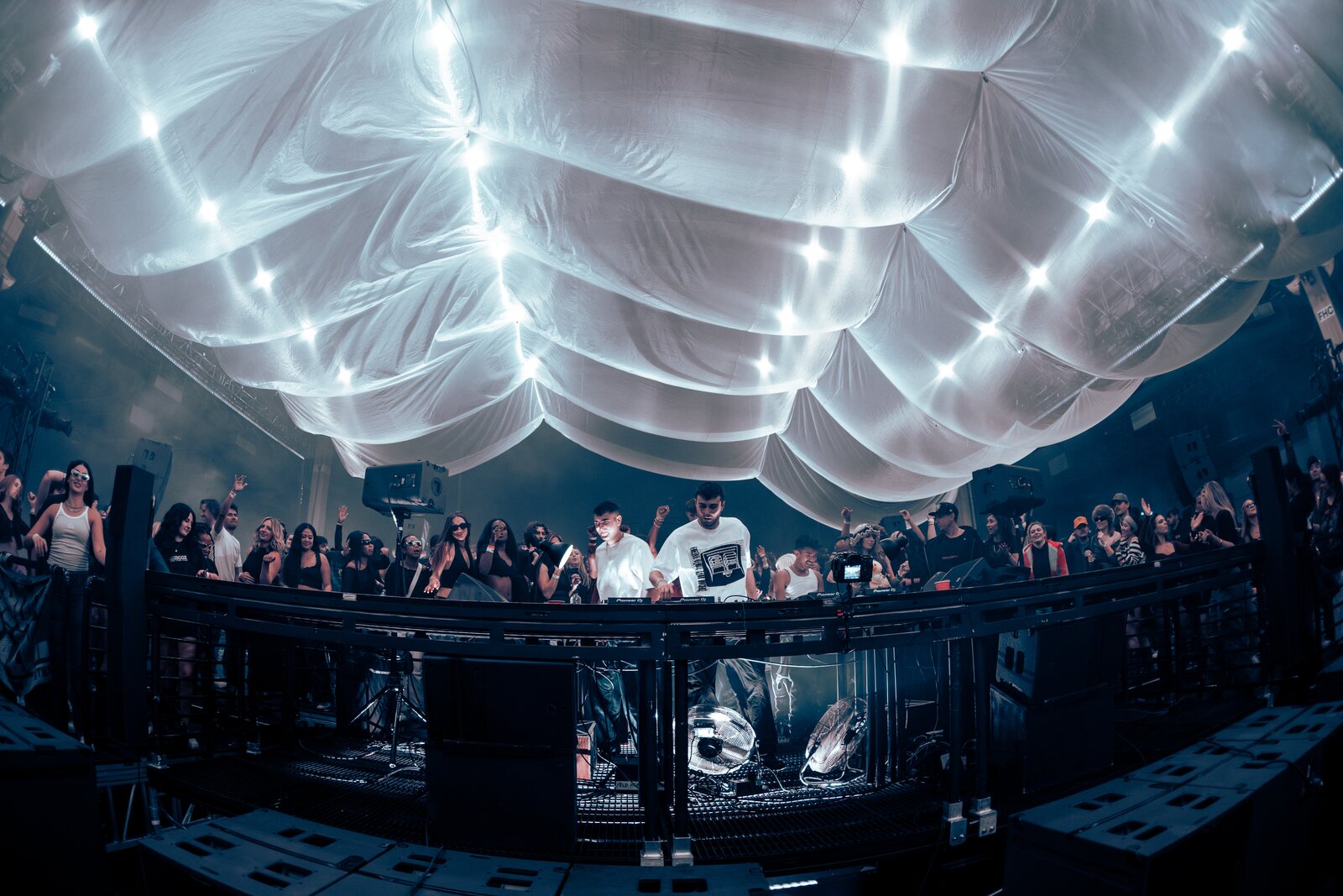 fred again performing at a central booth surrounded by a crowd under a fabric ceiling