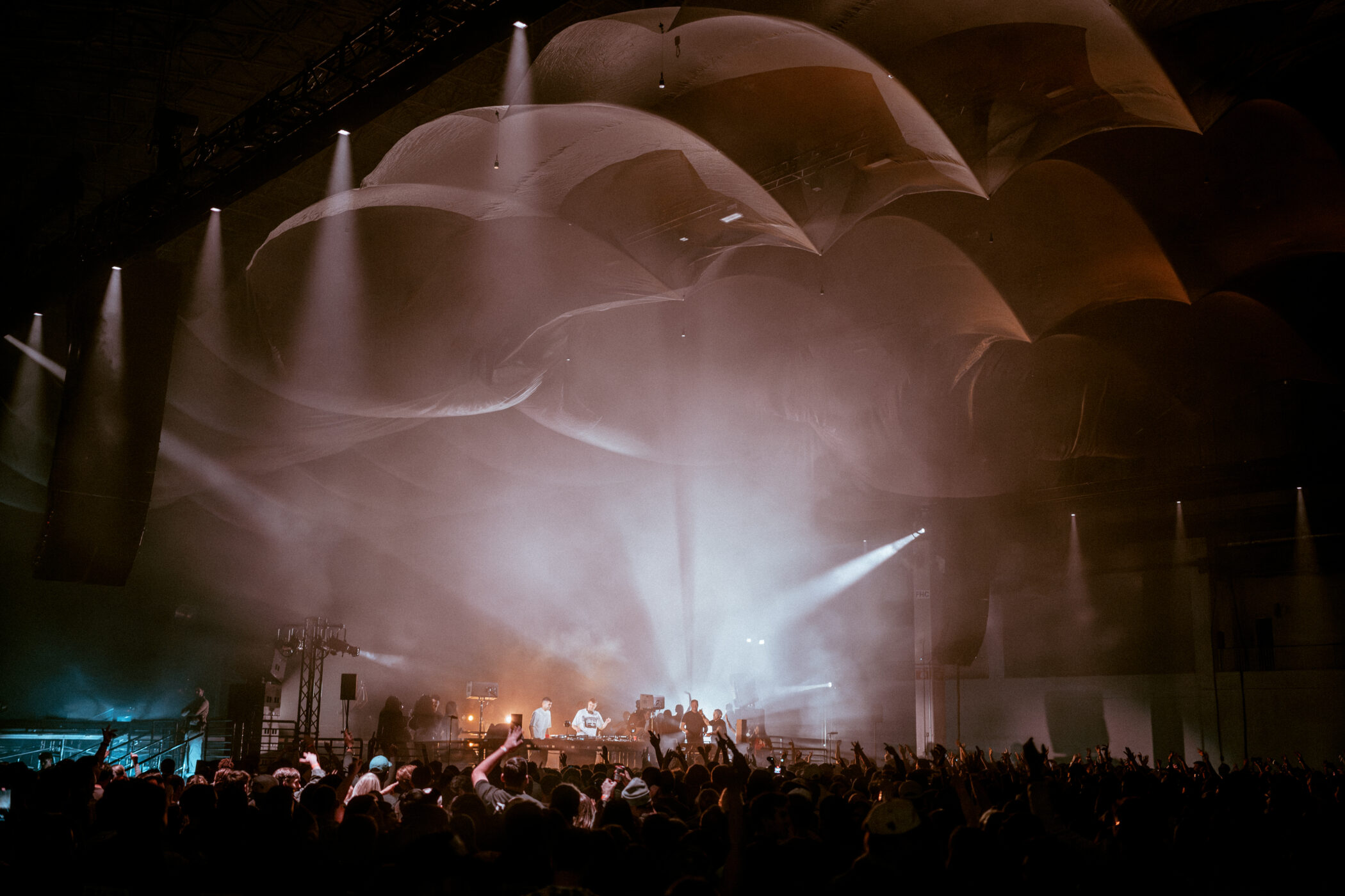 fred again concert crowd facing a DJ stage beneath large umbrella shaped fabric