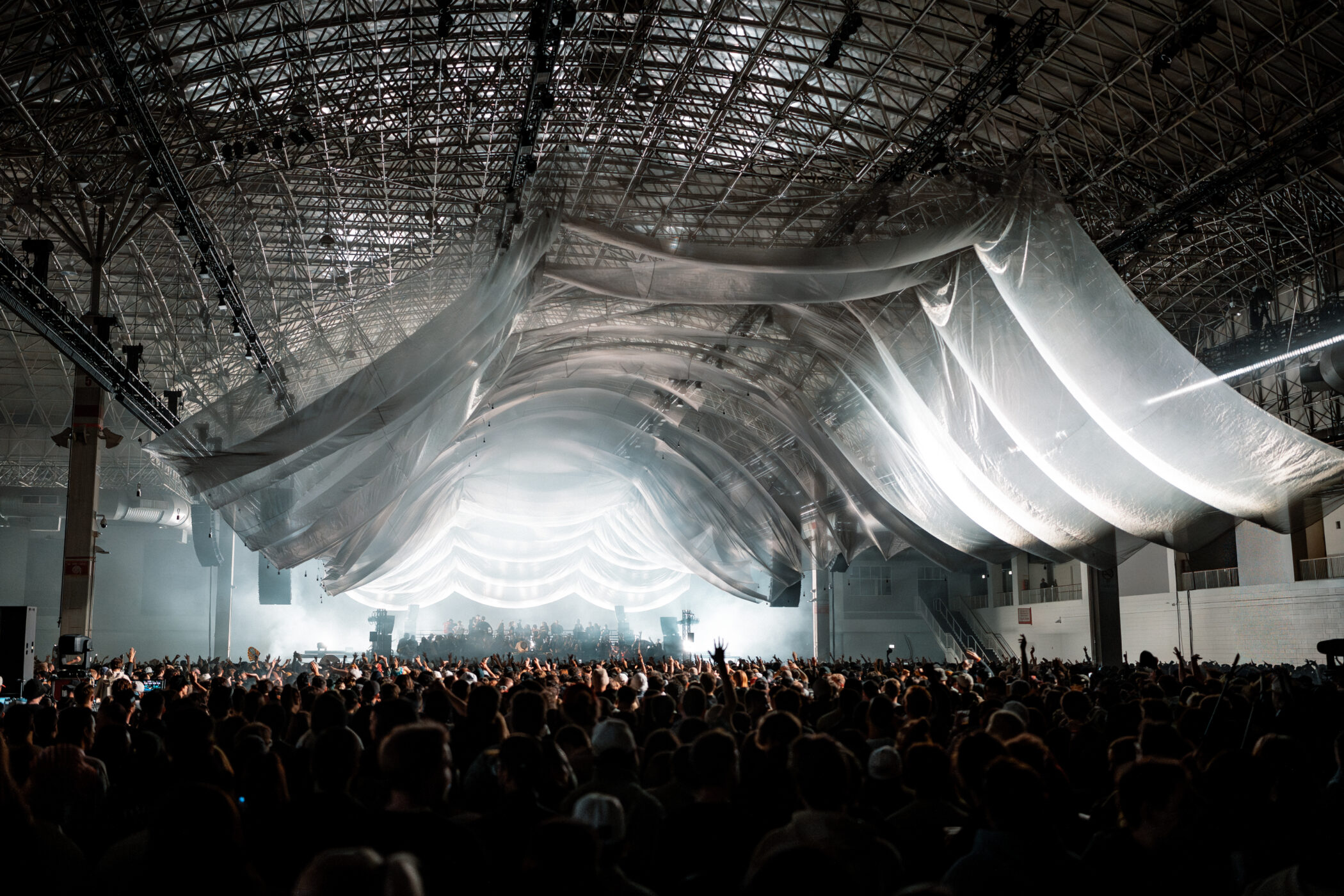 Indoor concert crowd under a large white fabric installation lit from the stage