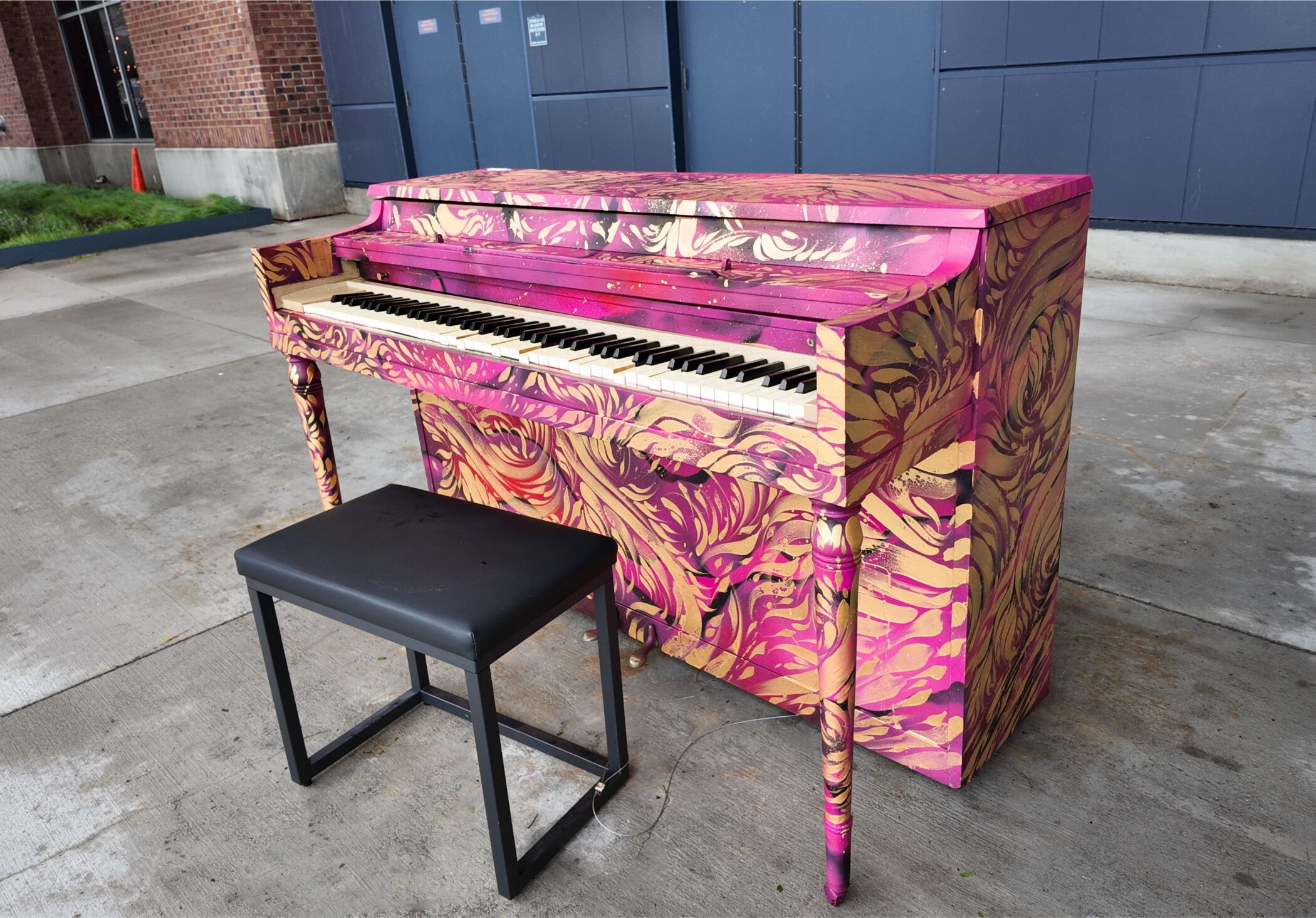 Street piano painted in pink and gold on a concrete plaza